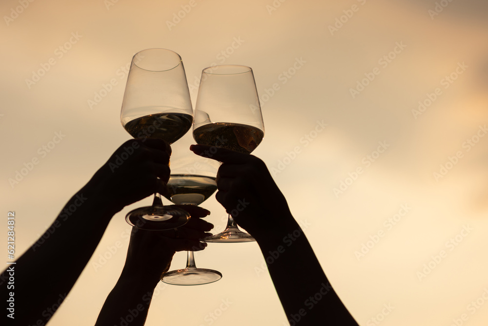 Group of friends with white wine in hands clinking with glasses. Close-up silhouettes of hands and drinks. Beautiful scenic sunset.