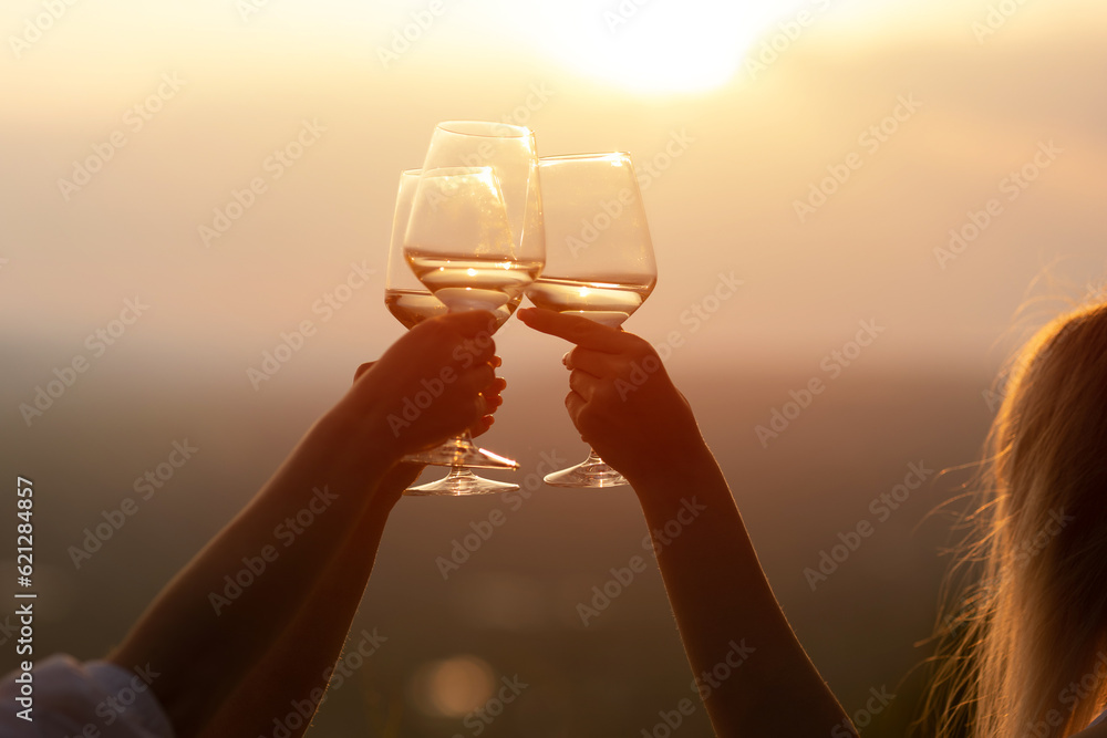 Clinking with wine glasses in beautiful background sunset. Hands of group of friends.