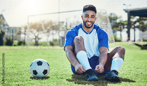 Sports, man or soccer player tie shoes for training, fitness games and performance on stadium field. Portrait, happy indian athlete or lace football sneakers on grass pitch to prepare for competition © Daniels C/peopleimages.com