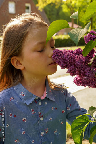 Cute girl in purple dress posing with lilac flowers. Portrait of little girl with lilac, spring mood. photo