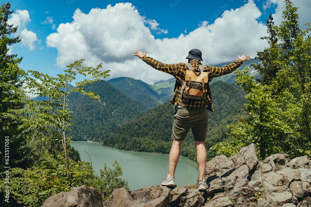 Obraz premium Hiking traveller man with backpack hands up enjoying beautioful view of Lake Ritsa in Abkhazia