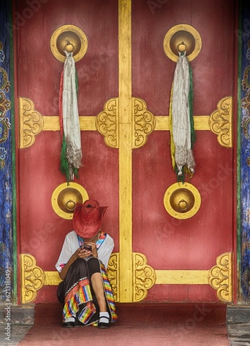 Tibetan girl checks her phone in front of an ornate buddhist temple door in Beijing 