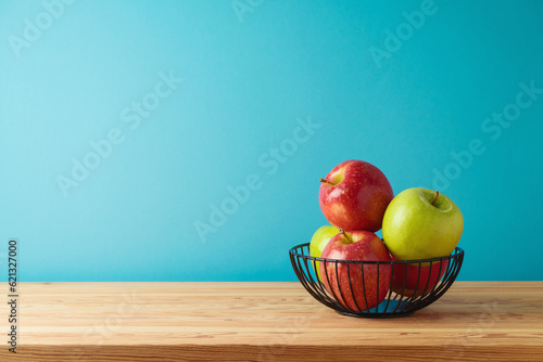 Red and green apples in metal basket on wooden table. Kitchen background