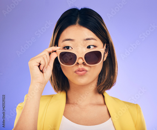 Fashion, sunglasses and a model asian woman on a purple background in studio for trendy style. Face, shades and attitude with a confident young female person looking over a stylish eyewear frame