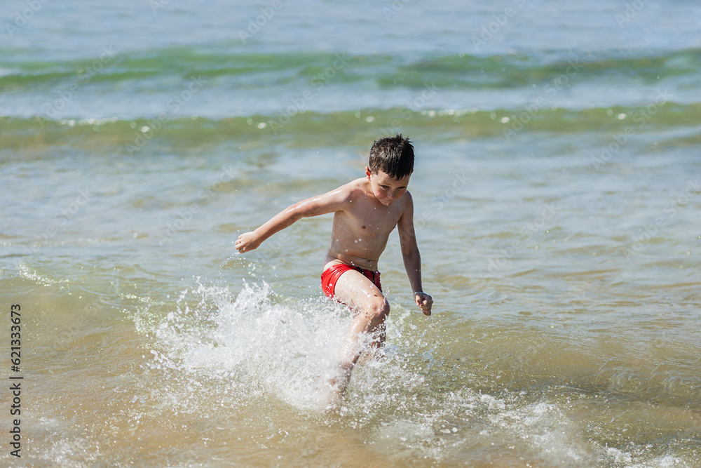 adorable school boy jumping in the water and enjoying the beach in summertime