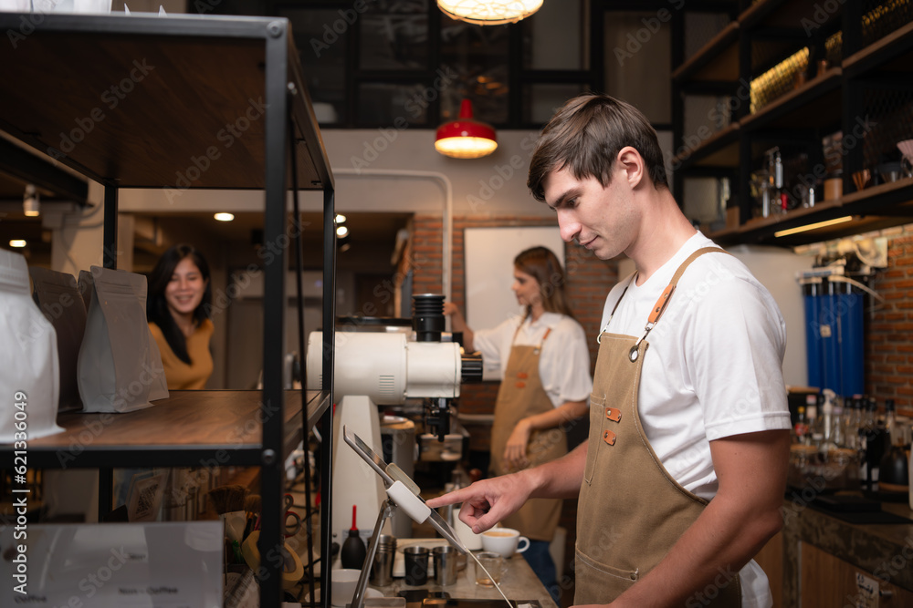 Portrait of a young male barista in apron using payment machine in cafe