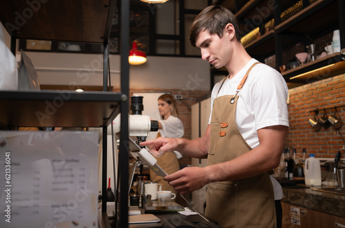 Portrait of a young male barista in apron using payment machine in cafe