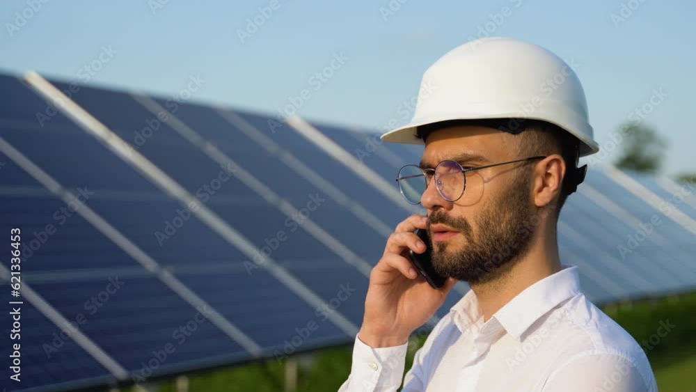 Confident engineer wearing safety hard hat, holding mobile phone, making a call. Engineer, worker, or architect working with Solar panel concept Confident engineer wearing safety hard hat, holding mobile phone, making a call. Engineer, worker, or architect working with Solar panel concept