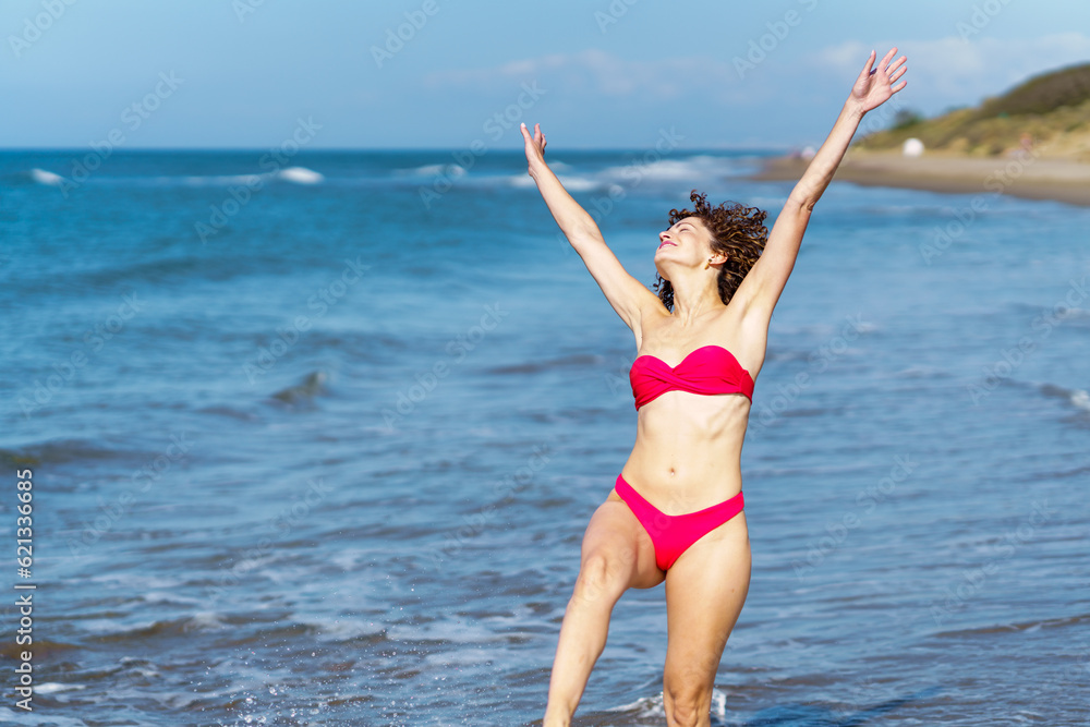 Carefree woman in bikini with raised arms at beach