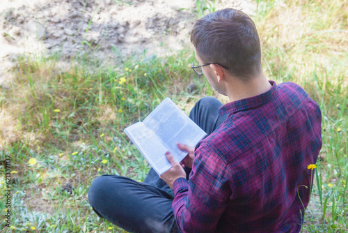 A man is reading a book in the park. Reading a book outdoors. Outdoor recreation