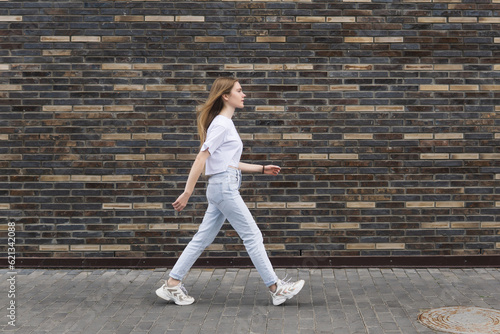 young woman walks down the street in front of a brick wall © Evgeny