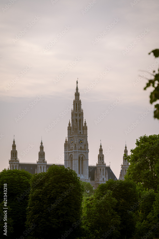 Vienna city hall tower beyond green trees during summer sunset