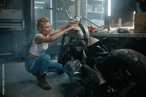 Young pretty woman mechanic polishing motorcycle after repair at workshop