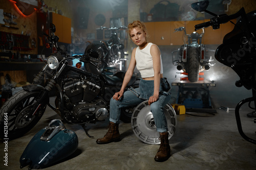 Young trendy blond woman mechanic at motorbike garage