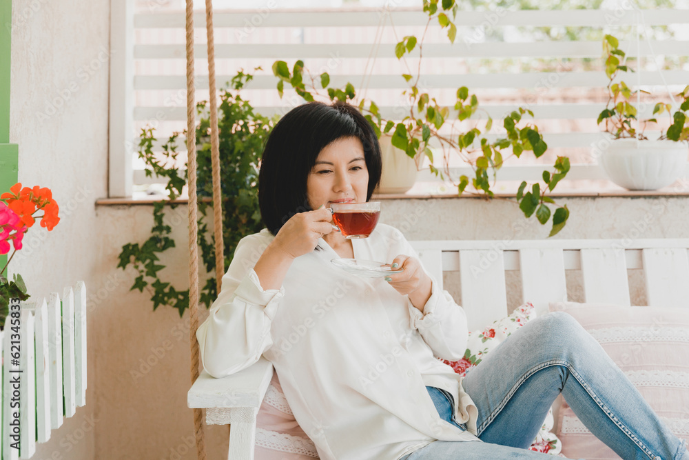 Portrait of an adult Asian woman drinking tea in a glass cup on the terrace of her house. Portrait of an adult Asian woman drinking tea in a glass cup on the terrace of her house.