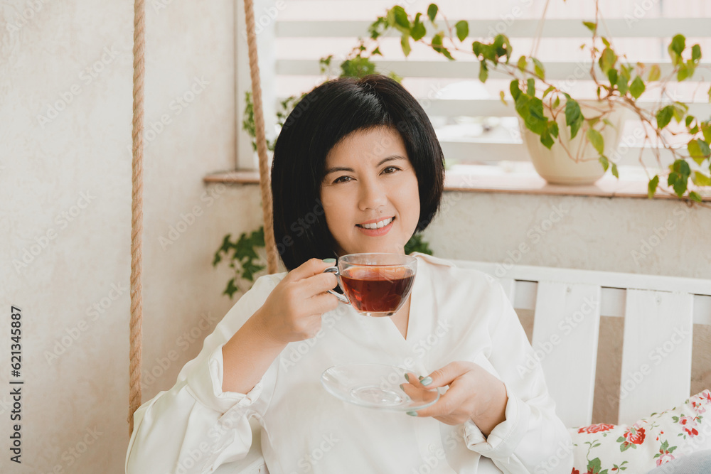 Portrait of an adult Asian woman drinking tea in a glass cup on the terrace of her house. Portrait of an adult Asian woman drinking tea in a glass cup on the terrace of her house.