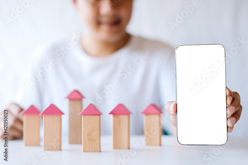 A young man is assembling a condo model while showing a blank white smartphone screen to fill in some text.