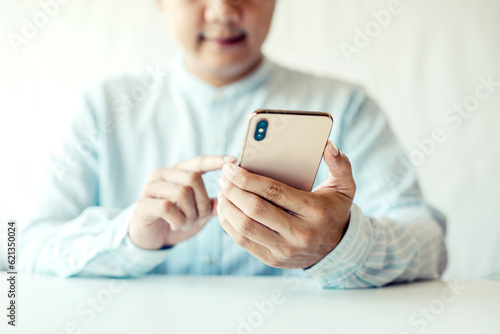 Cheerful businessmen use smartphones while sitting on the sofa at home. Handsome young asia man sitting on a couch reading messages on a mobile phone.