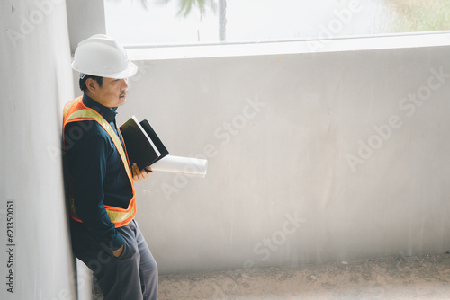 A foreman wearing a hard hat stands holding a blueprint. Supervising and inspecting the construction project of the building to be successful as planned.