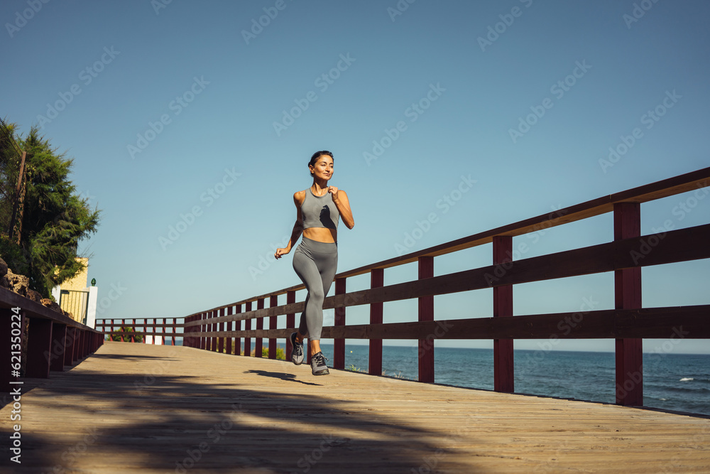 Fototapeta premium beautiful brunette girl in gray leggings runs on the seashore