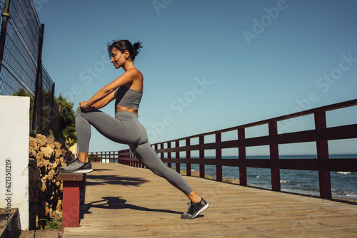 a beautiful brunette girl in gray leggings is warming up before running on the seashore
