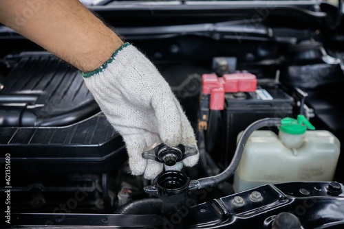 Close-up of hand of a gloved mechanic opening the radiator cap to check the coolant level. A man's hand is holding the radiator cap and opening it to check the water in the engine.