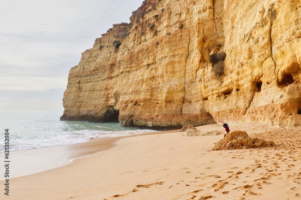 Teenage girl doing a handstand behin a rock on a sandy beach in southern Portugal on a sunny winter day.