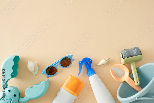 Children's sun protection cream concept. Top view flat lay of sunscreen sprays, eyeglasses, beach toys, seashells on pastel beige background with empty space for advert or text