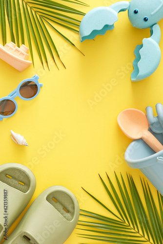 Summer coastal relaxation period for kids idea. Top view vertical photo of flip-flops, sandbox toys, sunglasses, palm leaves, seashell on yellow background with empty space for advert or message