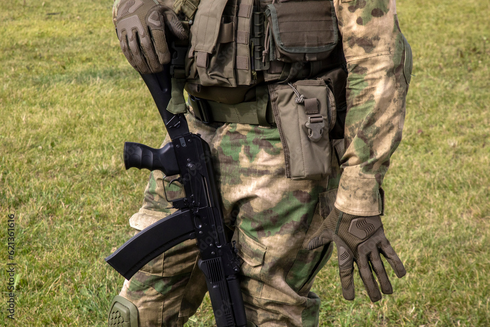 A soldier in uniform and with a weapon stands against a background of green grass A soldier in uniform and with a weapon stands against a background of green grass