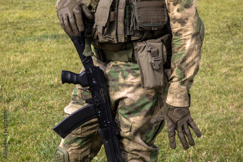 A soldier in uniform and with a weapon stands against a background of green grass