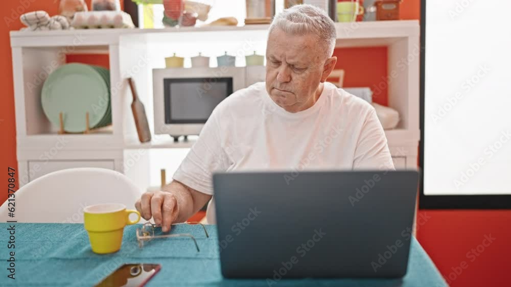 Middle age grey-haired man using laptop wearing glasses at dinning room Middle age grey-haired man using laptop wearing glasses at dinning room