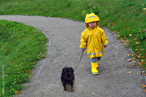 Little toddler boy walking with his dog in the rain
