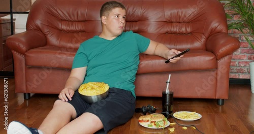 fat teenager boy is addicted to TV Slow motion overweight boy sit on sofa alone, has problems with nutrition, lead unhealthy lifestyle. laziness concept