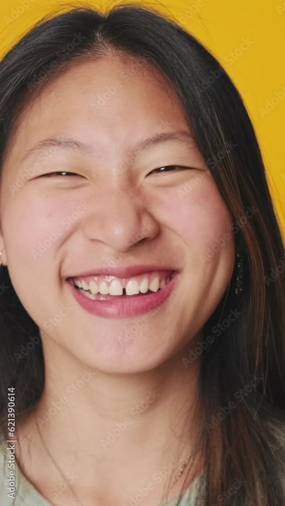 Close up, young woman looking at camera and laughing isolated over yellow background in studio Close up, young woman looking at camera and laughing isolated over yellow background in studio