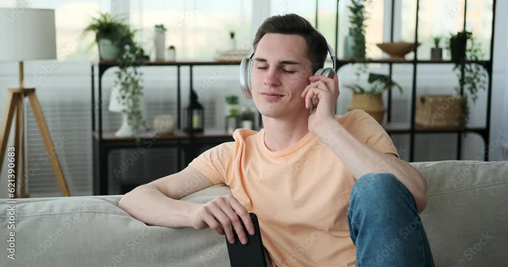A young man, brimming with positivity, with a bright smile adorning his face, he comfortably sits on the sofa in the cozy living room. He navigating through apps and messages. A young man, brimming with positivity, with a bright smile adorning his face, he comfortably sits on the sofa in the cozy living room. He navigating through apps and messages.