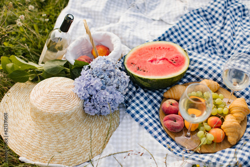 Breakfast picnic with croissants, fruits and flowers on a blanket on a sunny day. Picnic, food, brunch, summer mood.