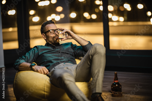 Young businessman sitting in bag chair and drinking cognac after successfull day on work