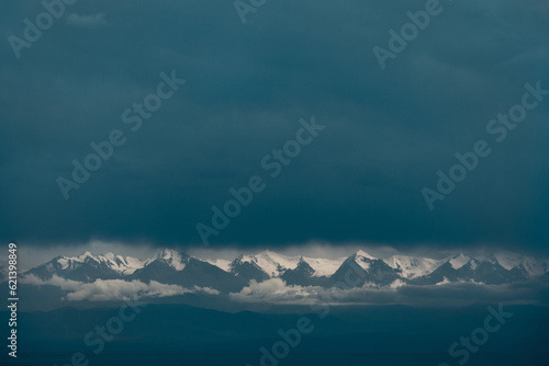 Picturesque dramatic landscape of snow-covered mountain tops amidst clouds and fog © chaossart