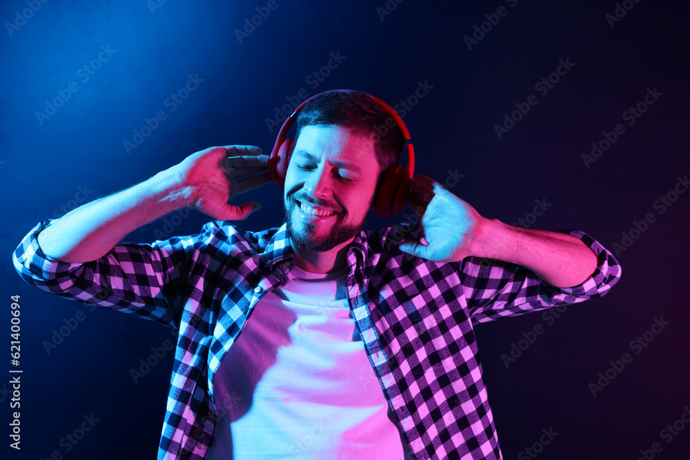 Happy man in headphones enjoying music in neon lights against dark blue background Happy man in headphones enjoying music in neon lights against dark blue background