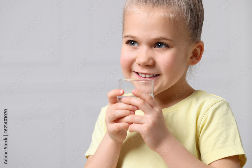 Happy little girl holding glass of fresh water on grey background, space for text Happy little girl holding glass of fresh water on grey background, space for text