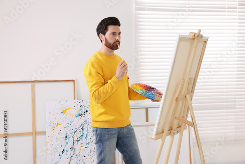 Man painting in studio. Using easel to hold canvas