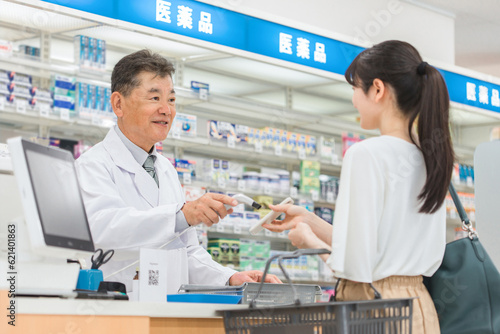 薬局でスマホ決済をする女性と薬剤師・調剤師の男性 