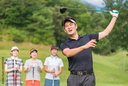 ゴルフ場でゴルフをする男性とスイングを見る女性ゴルファー 