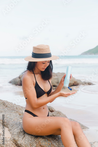 A responsible woman tourist wearing a bikini takes a moment to apply sunscreen, ensuring protection from the sun's rays during her beach vacation.