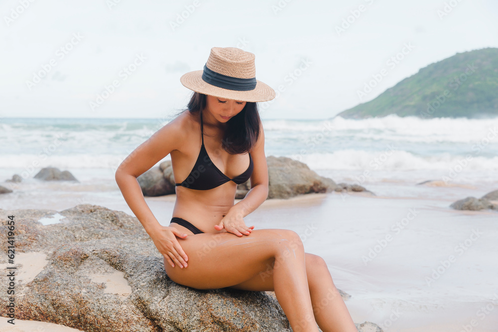 Taking sun care seriously, a woman tourist in a bikini applies sunscreen at the beach, safeguarding her skin from harmful UV rays. Taking sun care seriously, a woman tourist in a bikini applies sunscreen at the beach, safeguarding her skin from harmful UV rays.