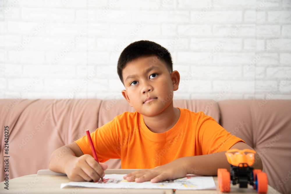 Little schoolboy writing in notebook at lesson. A boy doing his homework in the room. Little schoolboy writing in notebook at lesson. A boy doing his homework in the room.