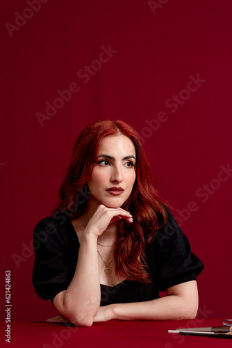Stylish red-haired woman posing against a red isolated background.