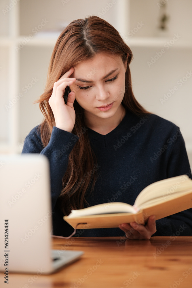 Thinking, A beautiful caucasian female student is studying remotely. She is sitting at a table at home with a laptop and a notepad and concentrated is watching a video conference. Thinking, A beautiful caucasian female student is studying remotely. She is sitting at a table at home with a laptop and a notepad and concentrated is watching a video conference.