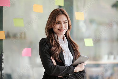 Successful businesswoman standing in creative office and looking at camera. Woman entrepreneur in a co-working space smiling. Portrait of beautiful business woman standing.